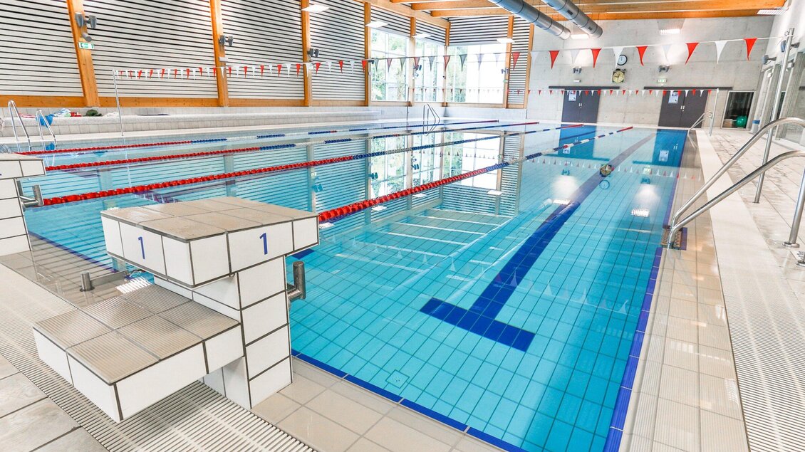Das Hallenbad der Sport Union Graz mit Startsockl und Schwimmbahnen mit bunten Fahnen. Die Bahnen sind deutlich markiert und die Umgebung ist hell und einladend. | © Harald Tauderer