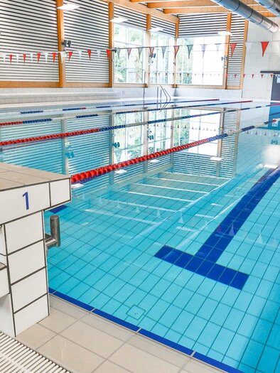 Das Hallenbad der Sport Union Graz mit Startsockl und Schwimmbahnen mit bunten Fahnen. Die Bahnen sind deutlich markiert und die Umgebung ist hell und einladend. | © Harald Tauderer