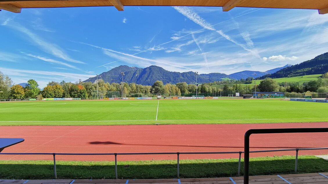 Ein weites Fußballfeld mit grünem Rasen und einer roten Laufbahn. Im Hintergrund sind Berge und ein klarer blauer Himmel zu sehen. | © Marktgemeinde Stainach-Pürgg
