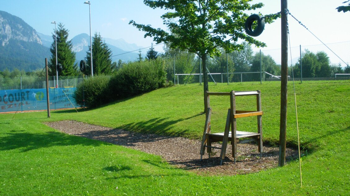 Ein Spielplatz in einer grünen Wiese mit einem Holzstuhl und einem Reifen zum Schaukeln. Im Hintergrund sind Bäume und Berge zu sehen. | © Marktgemeinde Stainach-Pürgg