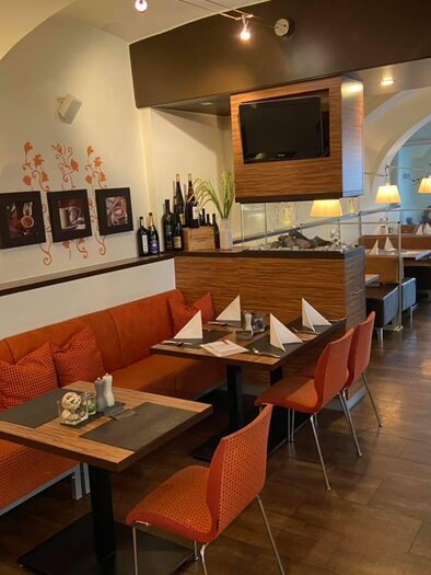 A cozy restaurant with orange seats and elegant tables. Artwork adorns the walls and an inviting atmosphere conveys a modern ambiance.