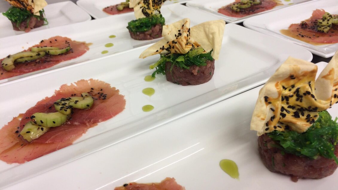 Ein elegantes Gericht auf weißen Tellern, bestehend aus Rindfleisch-Tartar, frischem Gemüse und knusprigen Elementen. Die Anordnung ist kunstvoll und ansprechend.