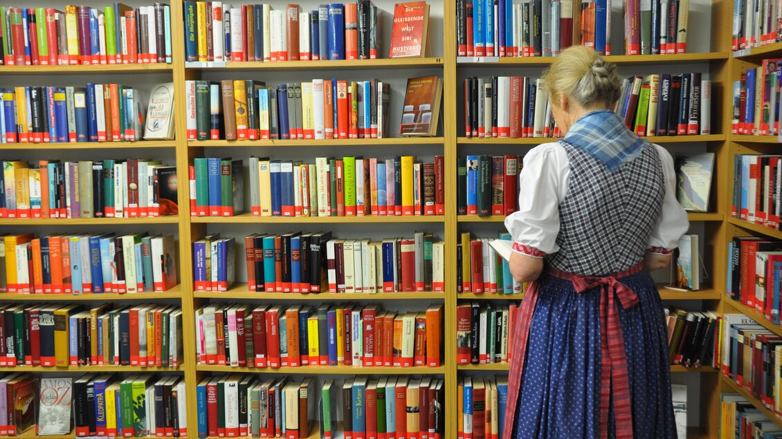 Eine Frau in traditioneller Kleidung steht vor einem Bücherregal. Im Hintergrund sind viele farbige Bücher sichtbar. | © Stadtgemeinde Bad Aussee