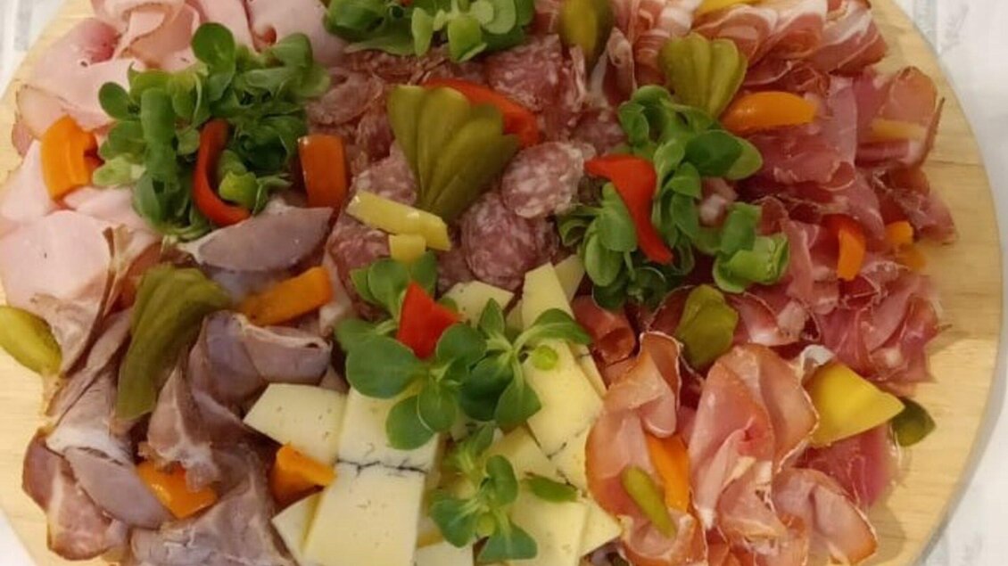 Eine Auswahl an Wurst- und Käsesorten auf einem Holzbrett, umgeben von frischen Kräutern und buntem Gemüse. Perfekt für ein herzhaftes Buffet oder als Appetizer. | © Mach Genussprodukte GmbH - Julia Trenker