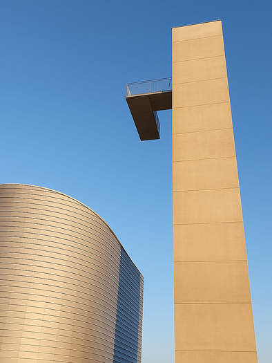 Ein modernes Gebäude mit geschwungener Fassade und einem hohen Turm. Der Himmel ist klar und blau. | © ChatGPT