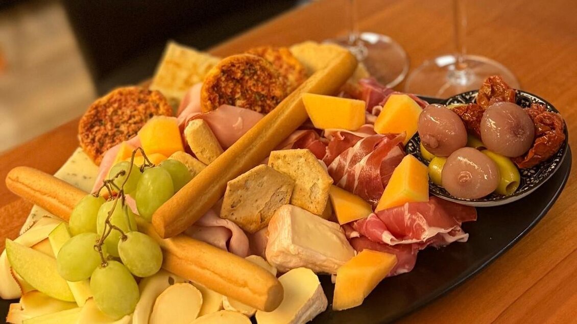 Eine appetitliche Auswahl an Käse, Wurst und Oliven auf einem Teller. Dazu gibt es Trauben und Brotstangen, perfekt für einen Snack. | © TV Südsteiermark - Elvira Kos-Czerniecki