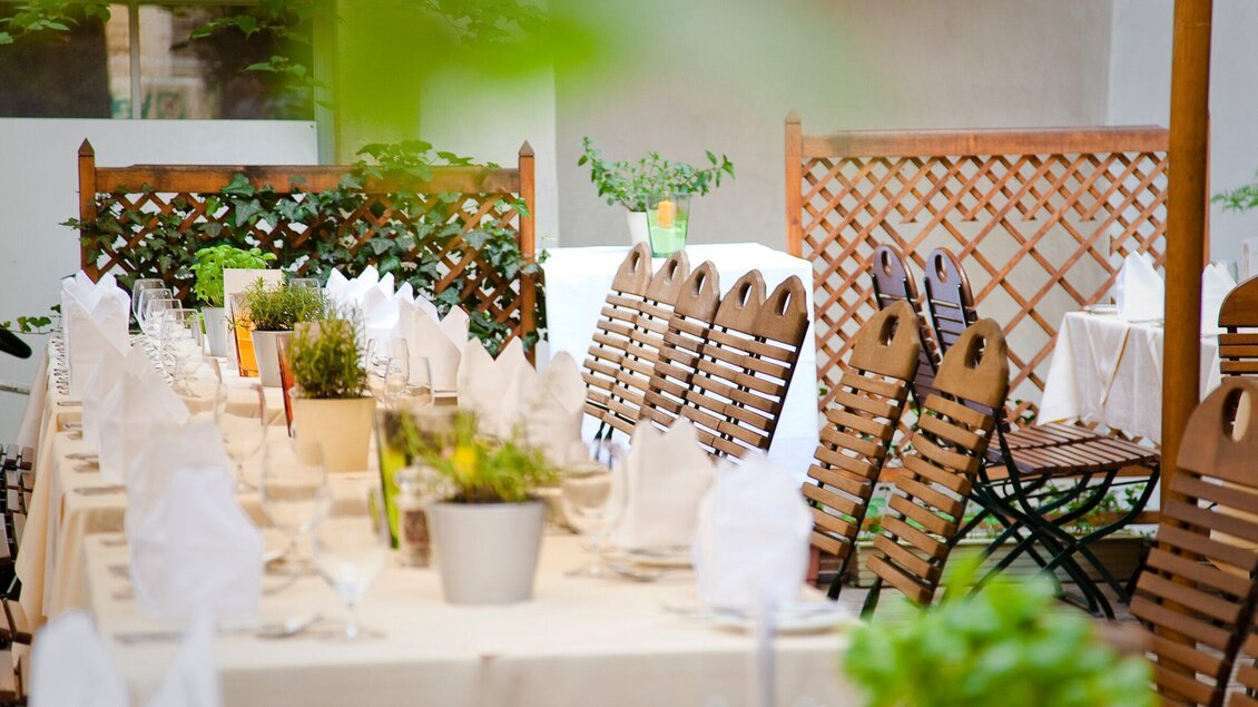 Ein schön gedeckter Tisch im Freien, umgeben von Pflanzen. Die Sessel sind aus Holz und die Atmosphäre ist einladend. | © Stainzerbauer