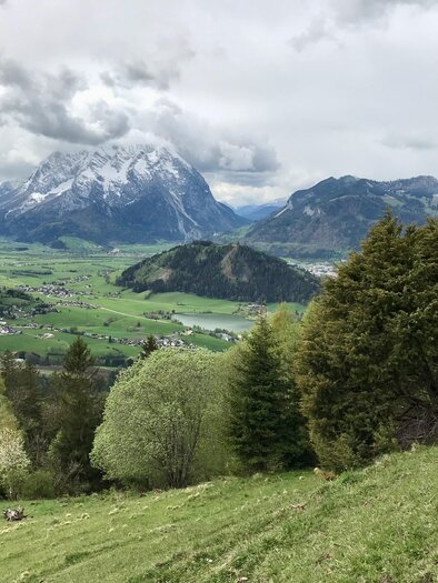 A picturesque mountainous landscape with green meadows and snow-capped peaks. In the background, a tranquil valley with a small village can be seen. | © Sabine Schulz