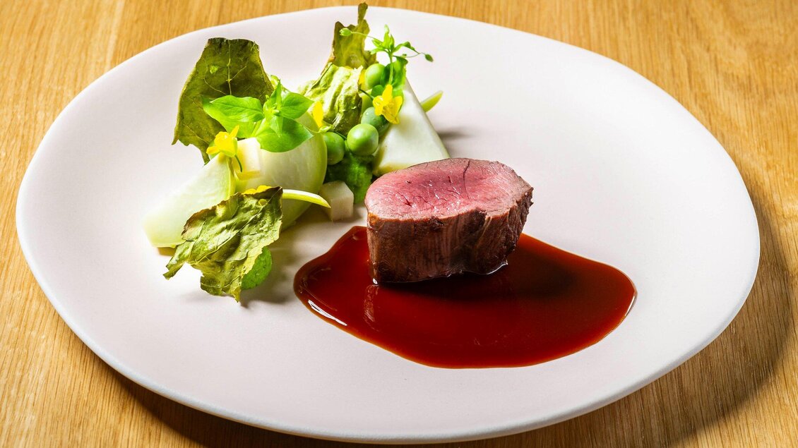 Ein elegantes Gericht mit einem zarten Stück Fleisch, serviert auf einer weißen Fläche. Dazu frischer Salat und eine dunkle Sauce. | © Stammtisch - Paul Stajan