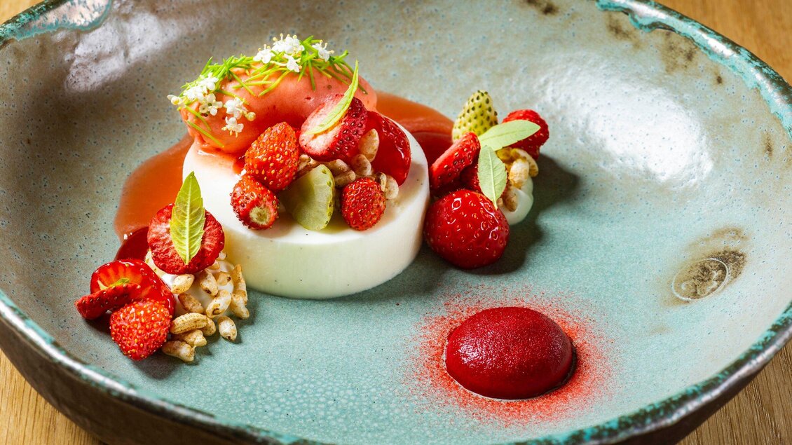 Ein elegantes Dessert auf einem kunstvollen Teller. Es besteht aus Panna Cotta mit frischen Erdbeeren und einer Himbeersauce. | © Stammtisch - Paul Stajan