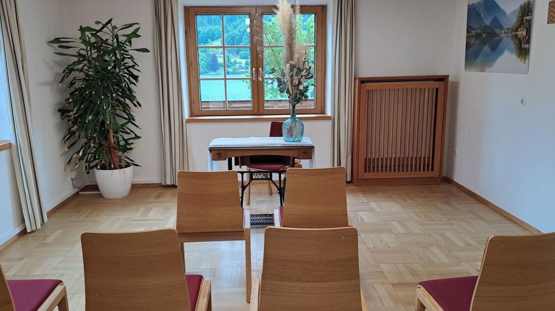 Ein heller Raum mit einem Tisch und mehreren Stühlen. Durch das Fenster sieht man eine grüne Landschaft mit Bäumen und Bergen. | © Theresa Grill