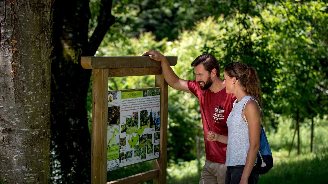 Ein Paar betrachtet eine Infotafel im Freien. Die Umgebung ist grün und sonnig, ideal für einen Ausflug in die Natur. | © Region Graz - Tom Lamm