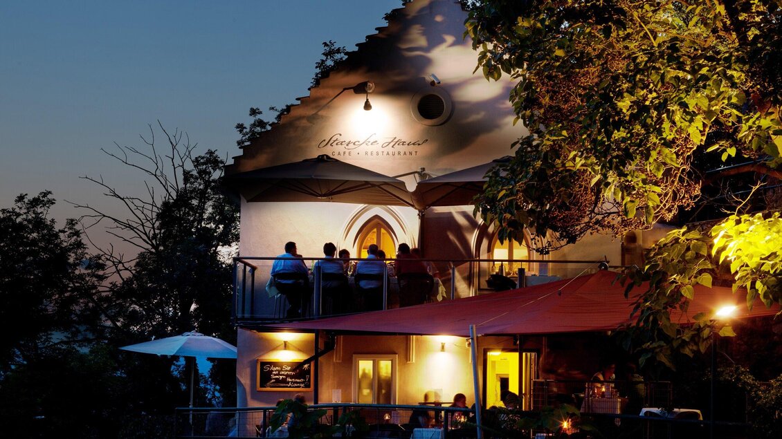 Ein charmantes Restaurant mit Außenbereich, beleuchtet von sanftem Licht. Bäume umrahmen die Szene und schaffen eine gemütliche Atmosphäre. | © Starcke Haus
