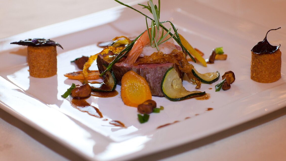 Ein kunstvoll angerichtetes Gericht mit einem Stück Fleisch und buntem Gemüse. Dekorative Beilagen und Kräuter runden das ansprechende Bild ab. | © Starcke Haus