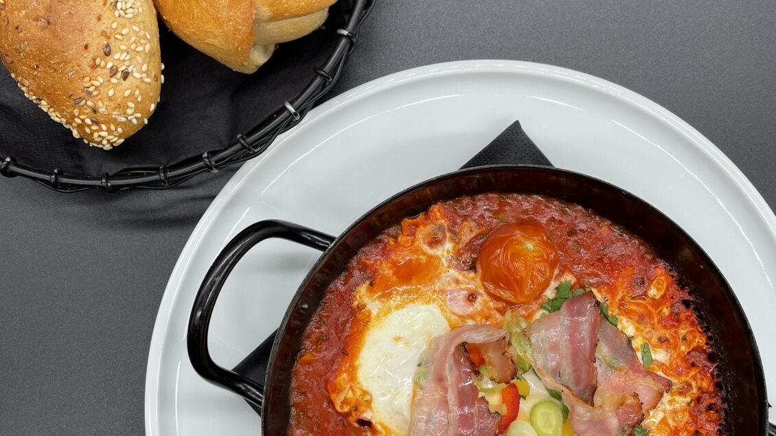 Ein herzhaftes Gericht in einer kleinen Pfanne mit Eiern, Schinken, Tomaten und Gemüse. Dazu frisches Brot auf einem kleinen Korb. | © Steffl-Bäck Sebastian Knapp