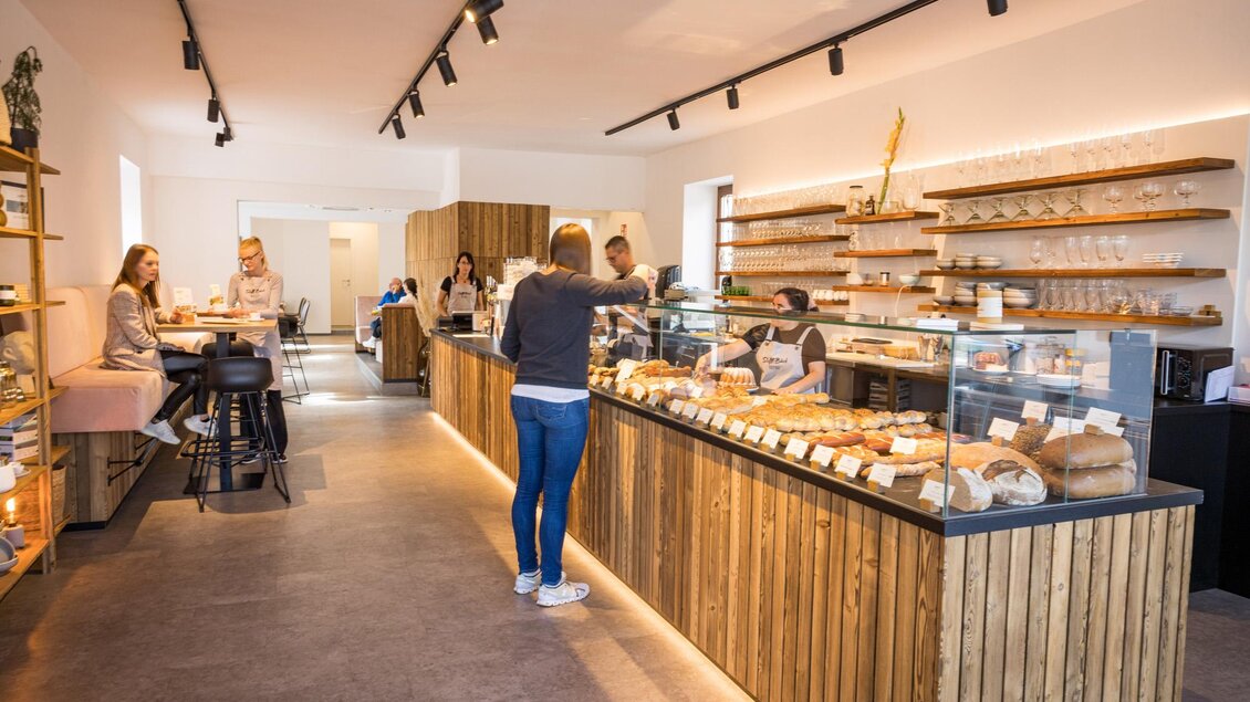Ein modernes Café mit Holzregalen und einer Theke voller frischer Backwaren. Gäste sitzen entspannt und genießen die gemütliche Atmosphäre. | © Netzwerk Kulinarik wildbild