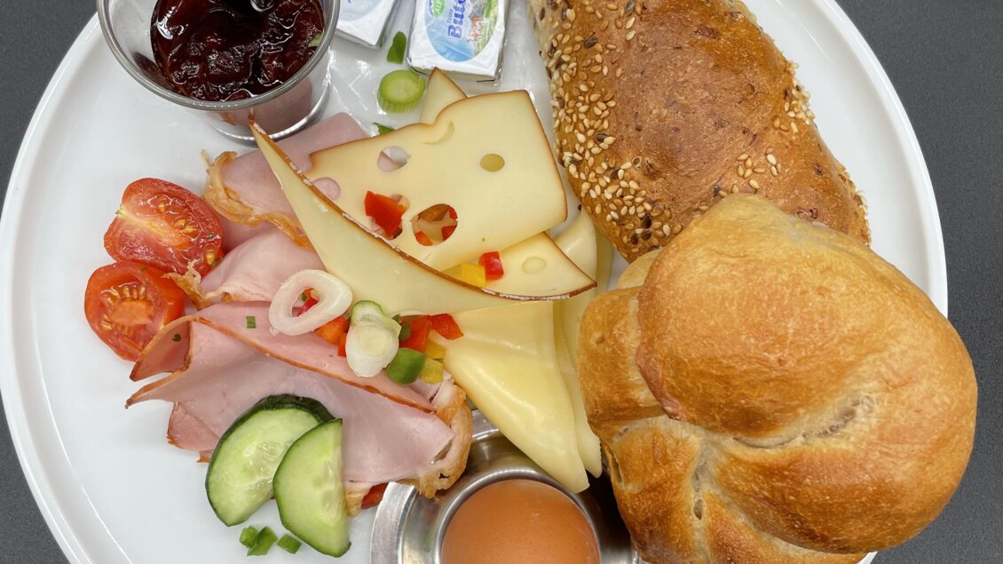 Ein Frühstücksteller mit verschiedenen Lebensmitteln. Darauf sind Brötchen, Käse, Wurst, frisches Gemüse, ein gekochtes Ei und Marmelade. | © Steffl-Bäck Sebastian Knapp
