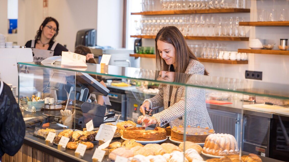 Eine freundliche Barista bereitet frische Backwaren an einer Theke vor. Im Hintergrund sind weitere Mitarbeiter und Gläser sichtbar. | © Netzwerk Kulinarik wildbild