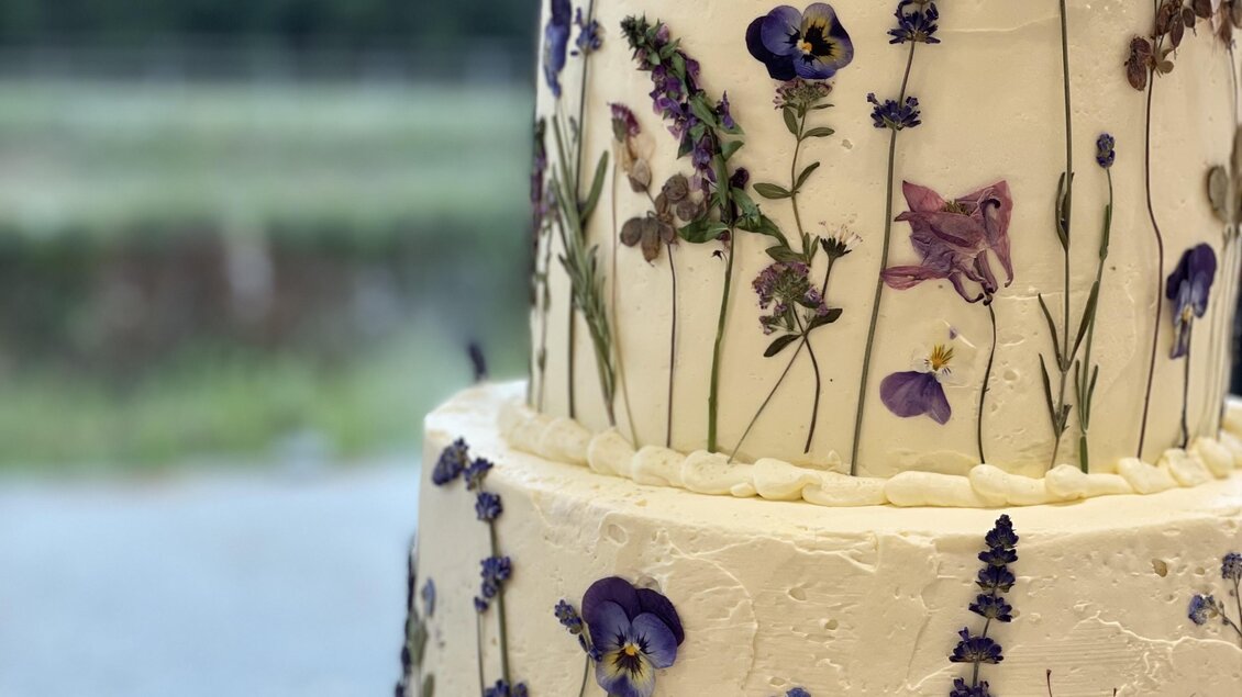 Eine elegante mehrstöckige Torte mit essbaren Blumen, die sie dekorieren. Im Hintergrund sind Bäume und ein klarer Himmel zu sehen. | © Steffl-Bäck Sebastian Knapp