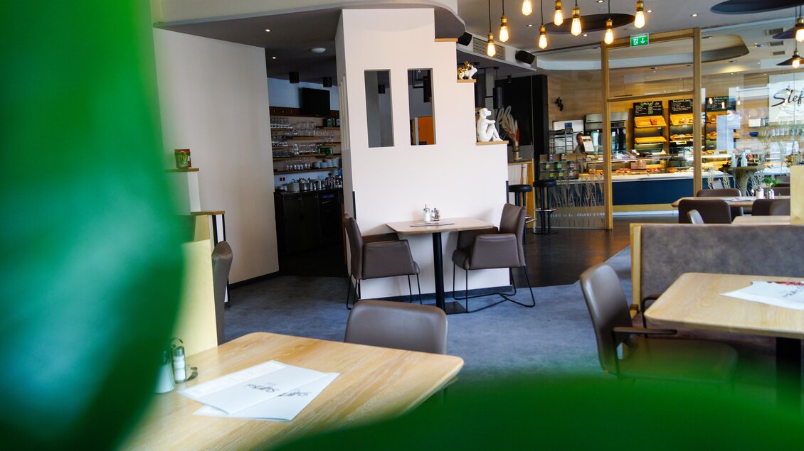 Ein modernes Restaurant mit Holz- und Designer-Möbeln. Im Hintergrund sind Lichtquellen und eine offene Küche zu sehen. | © Steffl-Bäck Sebastian Knapp