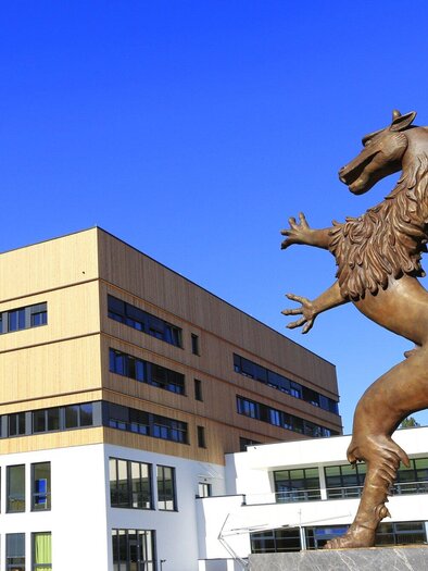 A statue of a lion stands in front of a modern building. The sky is clear and blue. | © Steiermarkhof - Foto Pachernegg