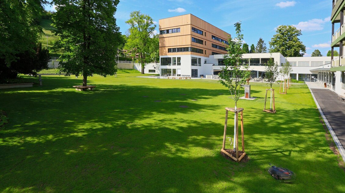 Ein gepflegter Park mit grünem Rasen und jungen Bäumen. Im Hintergrund ist ein modernes Gebäude zu sehen. | © Steiermarkhof - Foto Pachernegg