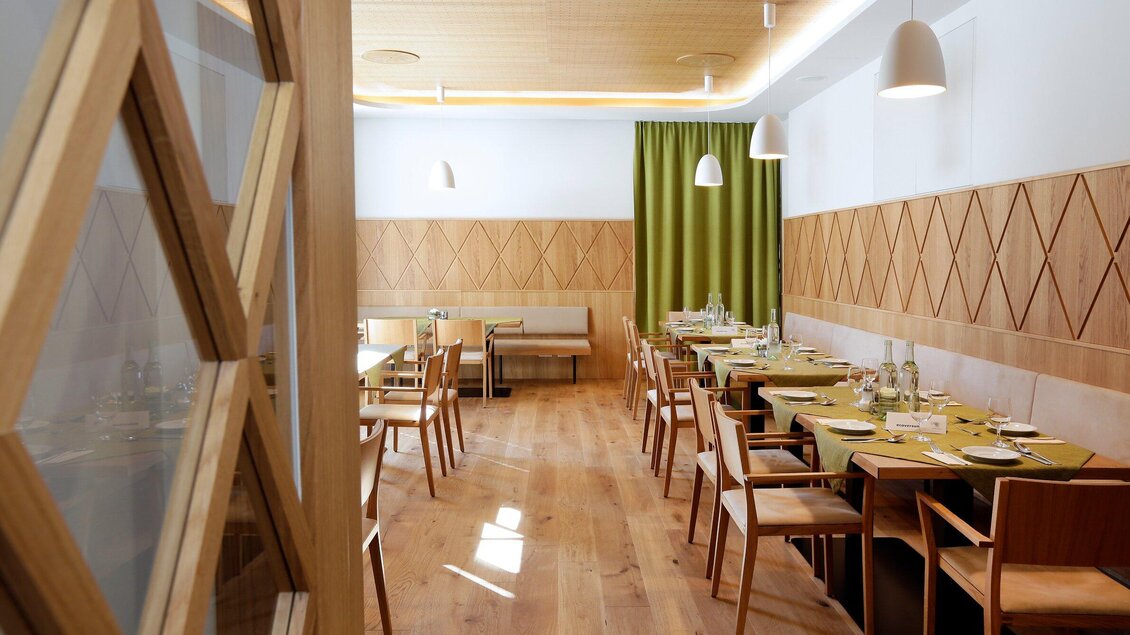 Ein modernes Restaurant mit Holzdecken und eleganter Einrichtung. Die Tische sind ordentlich gedeckt und es gibt große Fenster mit viel Tageslicht. | © Steiermarkhof - Foto Pachernegg