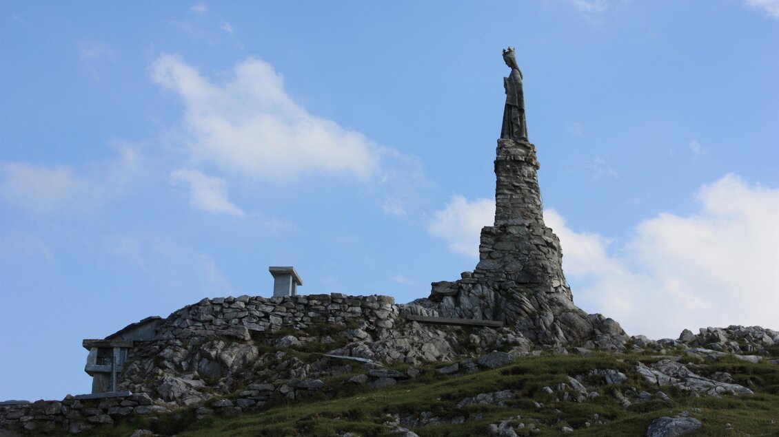 Ein Statue auf einem hohen Felsen mit einem klaren Himmel im Hintergrund. Die Landschaft besteht aus felsigem Terrain und sanften Hügeln. | © Willi Fuchs