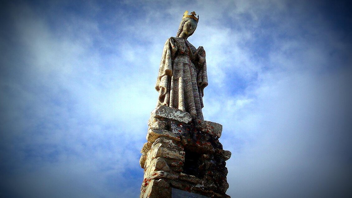 Eine hohe Statue steht auf einem Steinpodest. Der Himmel ist leicht bewölkt. | © Reinhold Waldaus