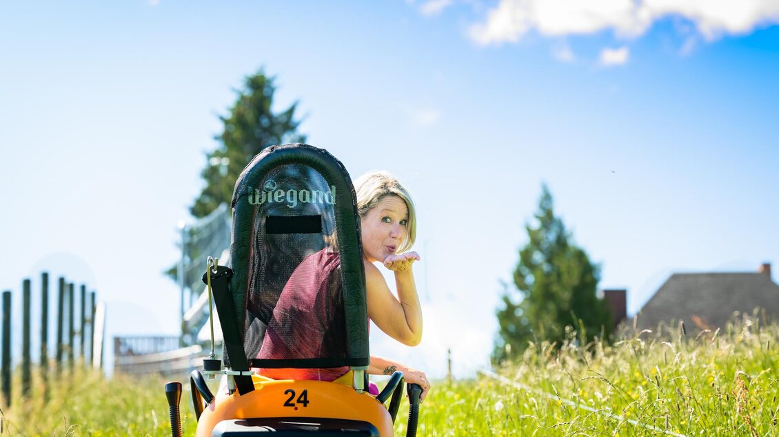 Ein Mädchen sitzt hinter einem kleinen Traktor in einer grünen Wiese. Im Hintergrund sind Bäume und ein blauer Himmel zu sehen. | © Region Graz - Mias Photart