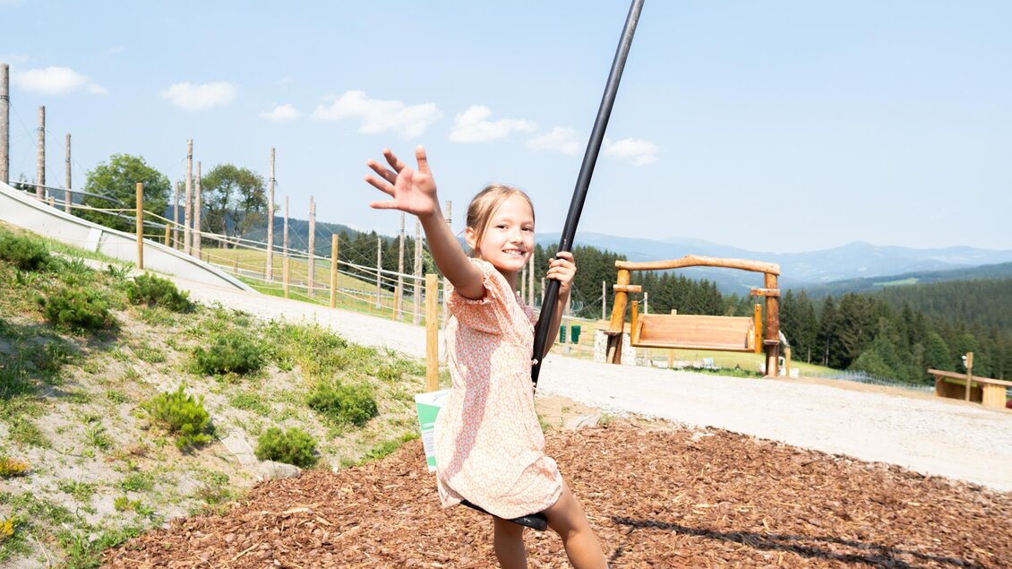Ein fröhliches Kind schwingt auf einer Seilbahn und winkt. Im Hintergrund sind Bäume und ein blauer Himmel zu sehen. | © Diesel