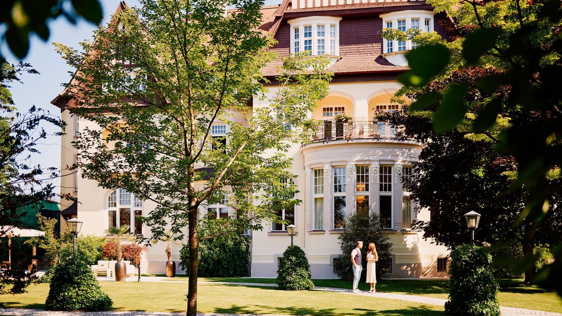 Ein wunderschönes Herrenhaus umgeben von einem gepflegten Garten. Zwei Personen stehen vor der Fassade und genießen die sonnige Atmosphäre. | © Tauroa GmbH