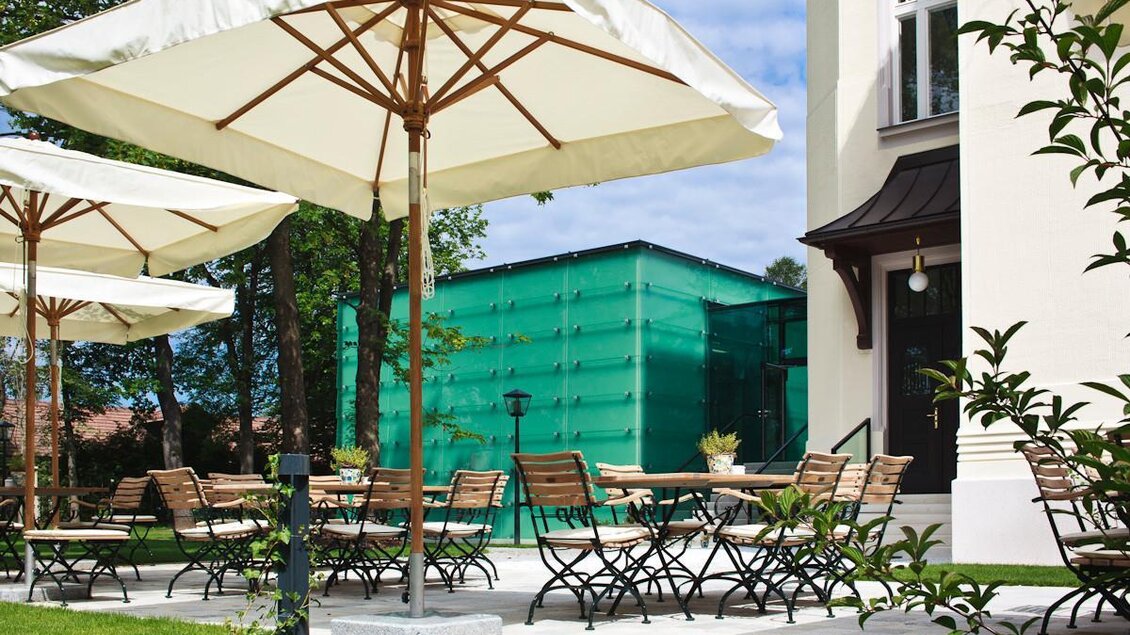 Ein gemütlicher Außenbereich mit Holzstühlen und großen Sonnenschirmen. Im Hintergrund ist ein grünes Gebäude zu sehen. | © Steirerschlössl