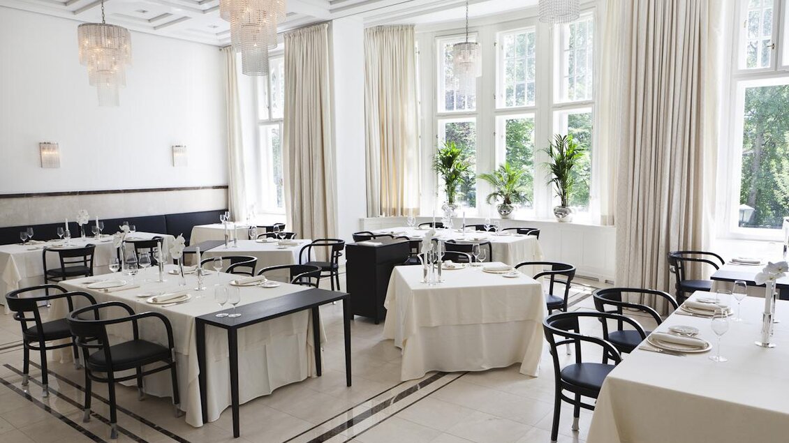 Ein elegantes Restaurant mit weiß gedeckten Tischen und modernen Stühlen. Große Fenster sorgen für viel Tageslicht und eine angenehme Atmosphäre. | © Steirerschlössl