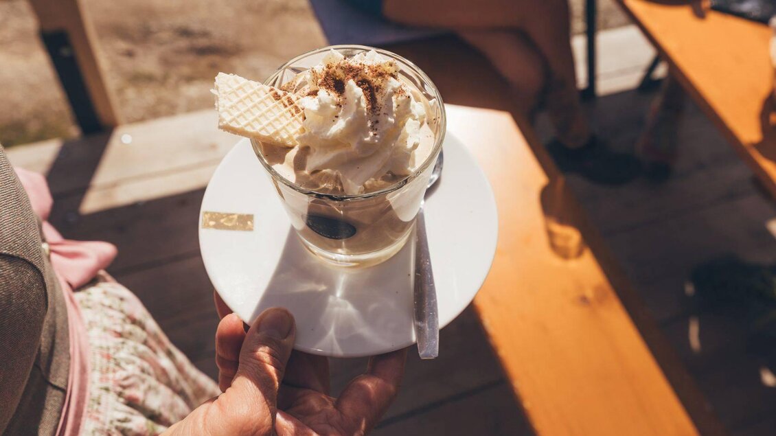 Ein leckerer Eisbecher mit Sahne und Waffel in einem Glas. Er wird auf einem weißen Teller serviert und von einer Hand gehalten. | © Krewenka