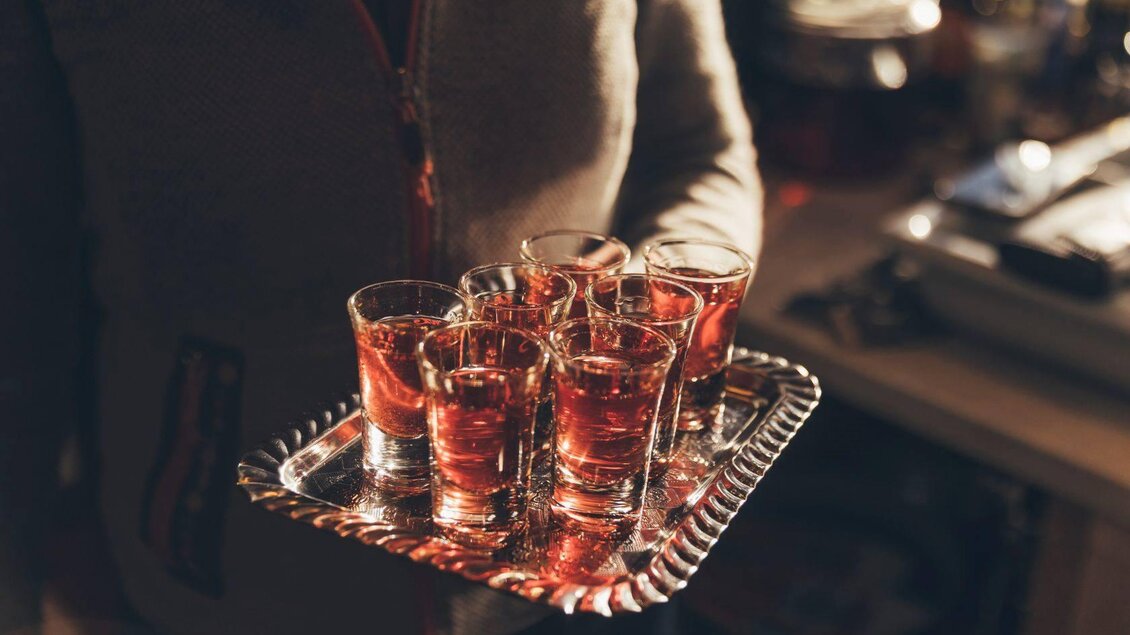 Ein Tablett mit mehreren Schnapsgläsern, gefüllt mit rotem Getränk. Im Hintergrund sind verschwommene Gegenstände zu sehen. | © Krewenka
