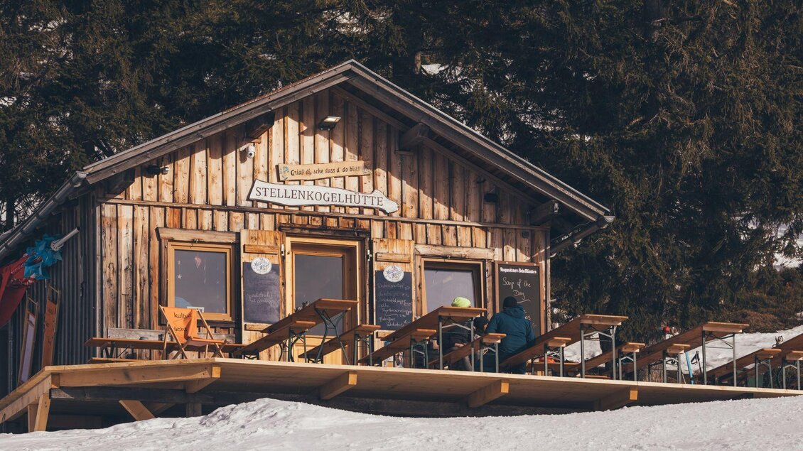 Eine gemütliche Skihütte aus Holz, umgeben von Schnee. Tische und Stühle stehen auf der Terrasse, ideal für eine Pause nach dem Skifahren. | ©  Krewenka