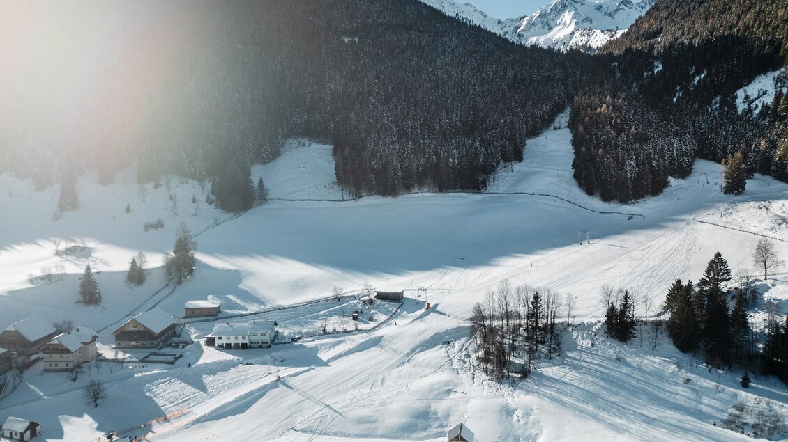 Ein malerischer Winterlandschaft mit schneebedeckten Hügeln und Bergen im Hintergrund. Kleine Hütten sind zwischen der glitzernden Schneedecke verteilt. | © Christoph Lukas
