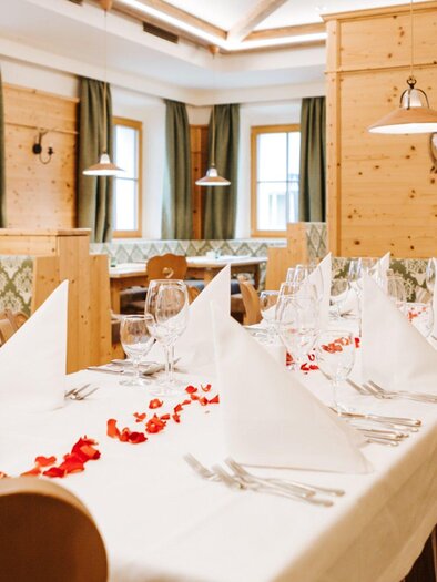 Ein gemütliches Restaurant mit Holzdekor und stilvoll gedeckten Tischen. Die Dekoration umfasst Servietten und Blütenblätter auf dem Tisch. | © Hotel Restaurant Stockinger