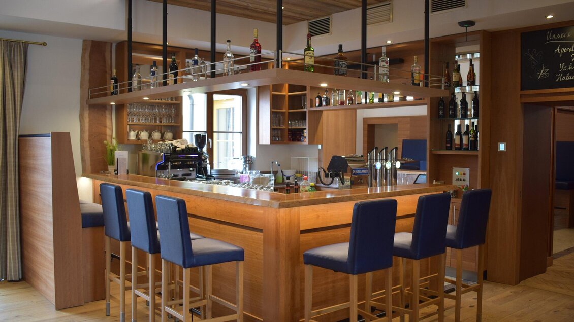 Eine elegante Bar aus Holz mit modernen Stühlen. Im Hintergrund sind verschiedene Getränkeflaschen und Gläser sichtbar. | © Hotel Restaurant Stockinger