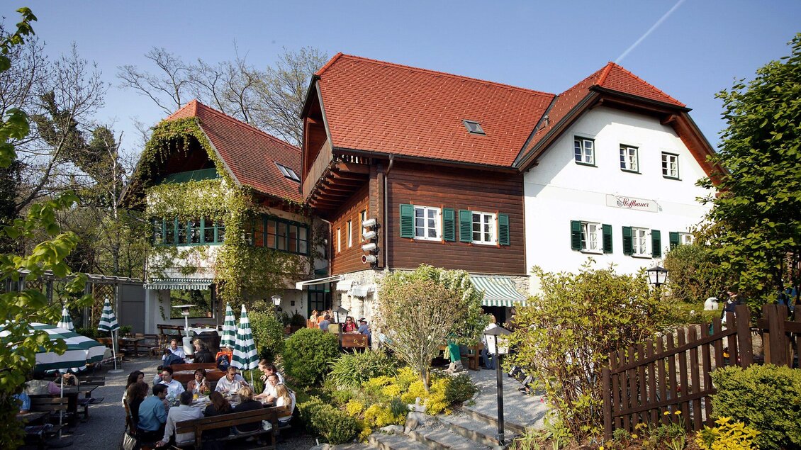 Ein gemütliches Restaurant mit traditionellen Gebäuden und einem schönen Außenbereich. Gäste sitzen entspannt im Freien unter Bäumen. | © Stoffbauer