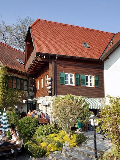 A cozy restaurant with traditional buildings and a beautiful outdoor area. Guests sit relaxed outside under trees. | © Stoffbauer