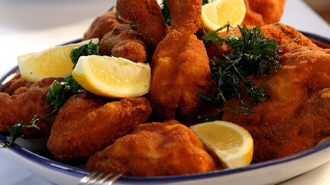 Ein Teller mit knusprigem frittiertem Hühnchen, garniert mit Zitronenscheiben und frischen Kräutern. Das Gericht sieht appetitlich und einladend aus. | © Stoffbauer