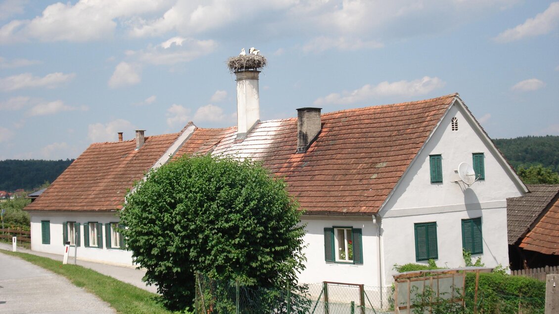 Ein weißes Haus mit einem roten Ziegeldach und grünen Fensterläden. Es steht in einer ländlichen Umgebung, umgeben von Bäumen und Wiesen. | © Kurkommission Bad Blumau