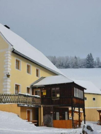 A charming yellow house in winter, surrounded by snow and snow-covered trees. On the porch stands a wooden pavilion that looks inviting. | © Stoxreiter