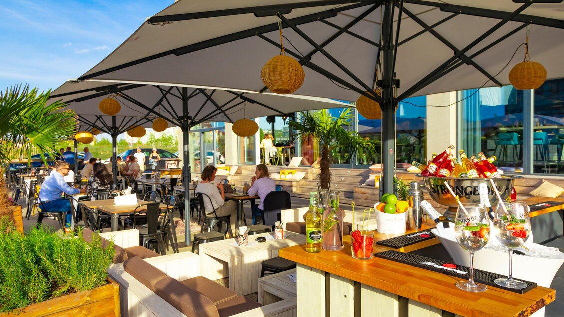 Eine einladende Terrasse mit Sonnenschirmen und gemütlichen Sitzgelegenheiten. Gäste genießen Speisen und Getränke in einer sonnigen Atmosphäre. | © Streets
