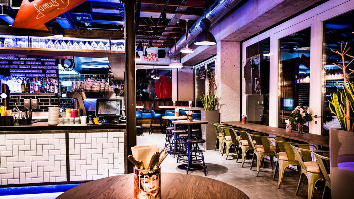 Eine moderne Bar mit stilvollem Interieur und einer angenehmen Beleuchtung. Tische und Stühle bieten Platz für Gäste in einem einladenden Ambiente. | © Streets - Werner Krug