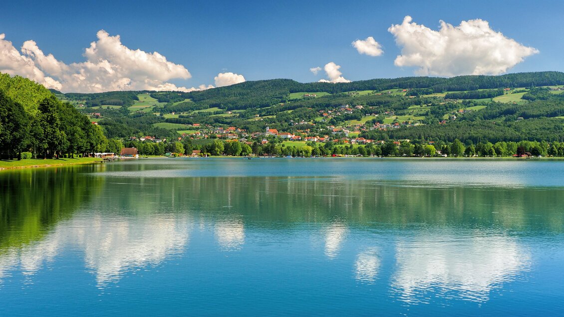 Ein ruhiger See umgeben von grünen Hügeln und Bäumen. Die Wolken spiegeln sich im Wasser, unter einem klaren blauen Himmel. | © Tourismusverband Oststeiermark