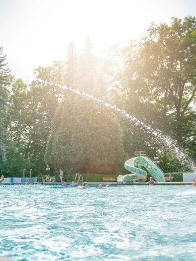 In the children's pool at Stukitzbad, there is a lot of activity. In the background, trees and a water slide can be seen. | © Holding Graz - Joel Kernasenko