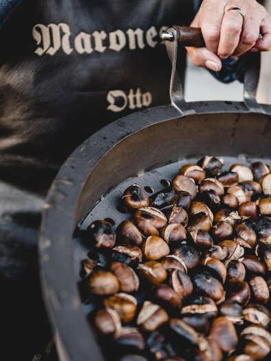 A vendor holds a large bowl of roasted chestnuts. The chestnuts are dark brown and shiny. | © Michaela Lorber